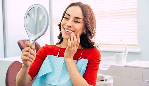 A woman admiring her dental implants in a hand mirror