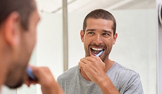 A man brushing his teeth while facing a mirror